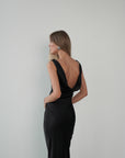 Woman wearing a black dress with a low back on a plain background